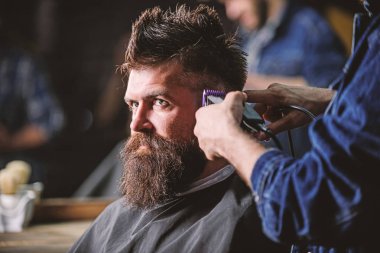 Eller berberin saç kesme makinesi ile kapatın. Hippi saç modeli almak istemci sakallı. Kuaför saç kesme makinesi ile çalışır. Salonların sandalye, koyu arka plan sakallı adam. Berber kavramı