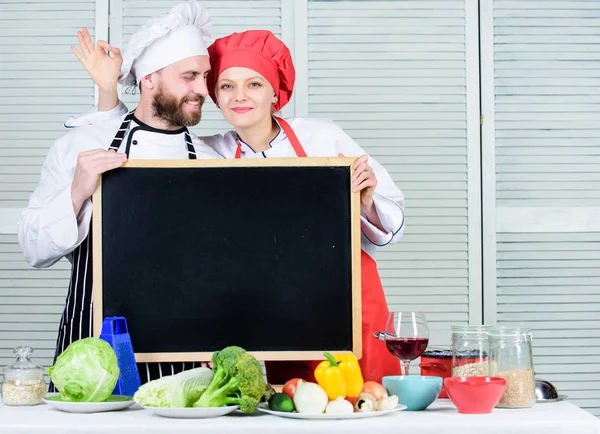 Lets make dinner together. Chef and cook helper gesturing ok sign at blackboard. Couple of man and girl at master class in cooking school. Master cook and prep cook teaching cooking class, copy space