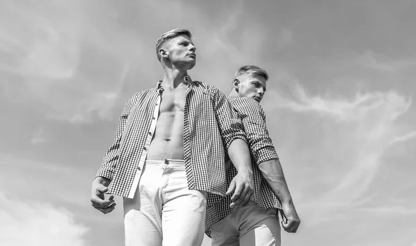 Menswear and fashion concept. Brothers twins looks attractive. Men strong athlete wear same shirts. Fashionable similar outfits. Men twins brothers muscular guys posing in shirts sky background