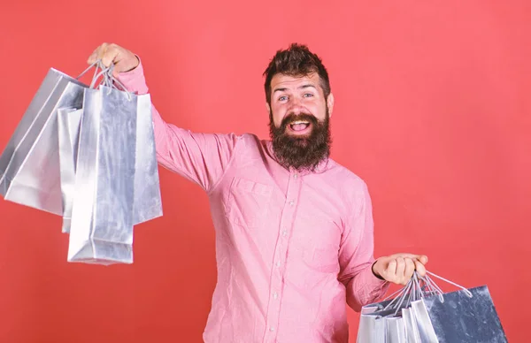 Ember, nagy mosollyal és szakáll gazdaság ezüst papír táskák, értékesítési koncepció. Szakállas férfi rózsaszín ingben, piros háttér. Csípő vidám arc és divatos szakáll és bajusz őrült a vásárlás — Stock Fotó