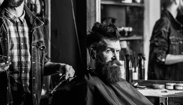 Barbiere con clipper e brutale cliente barbuto. Un cliente hipster che si taglia i capelli. Concetto di stile di vita hipster. Barbiere con tagliacapelli lavora su acconciatura per barbuto uomo barbiere sfondo — Foto Stock