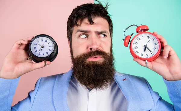 Guy unshaven puzzled face having problems with changing time. Changing time zones affect health. Time zone. Does changing clock mess with your health. Man bearded hipster hold two different clocks — Stock Photo, Image