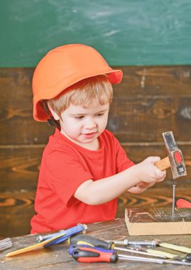 İşyeri güvenliği. Çivi çekiç turuncu kask içinde küçük bir çocuk. Sevimli çocuk araçları ile oynamak