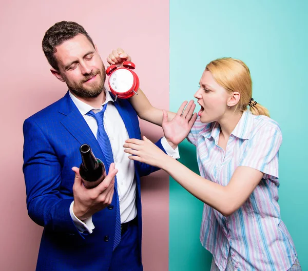 Atrapado por llegar tarde a casa. Hombre que sufre de alcoholismo. Esposa enojada conociendo al marido borracho tarde en casa. Empresario con botella de alcohol y mujer con reloj. Alcoholismo adictivo o abuso de alcohol —  Fotos de Stock