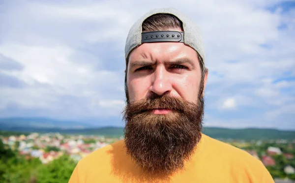 Elegante casual. Un hipster genial. Barbudo hombre en la moda hipster cap al aire libre. Un hombre brutal con barba larga y bigote. Hipster en ropa de moda callejera en el paisaje de verano — Foto de Stock