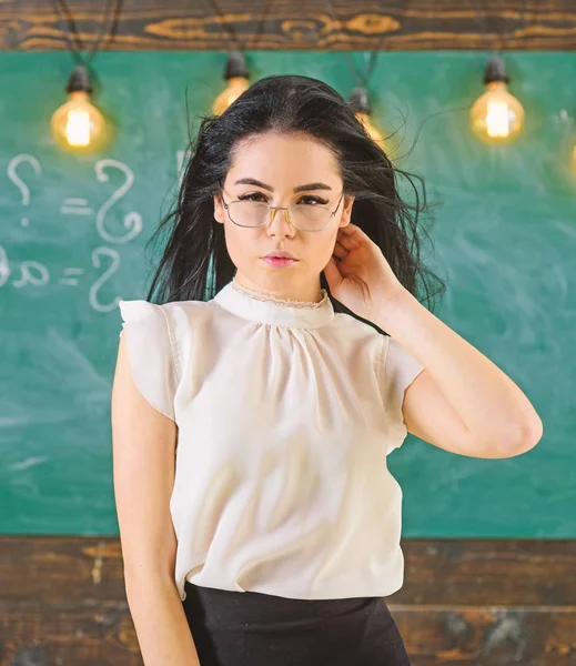 Vrouw met lange haren in witte blouse staat in de klas. De strenge leraar Lady op ontspannen gezicht staat voor schoolbord. Sexy leraar concept. Leraar met glazen en wapperende haren ziet er sexy — Stockfoto