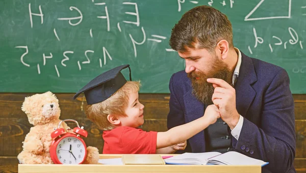 Far med skägg, lärare lär son, liten pojke, medan barn som slog honom. Kid glada boxning, slå pappa. Lekfulla barn koncept. Lärare och elev i mortarboard, svarta tavlan på bak — Stockfoto