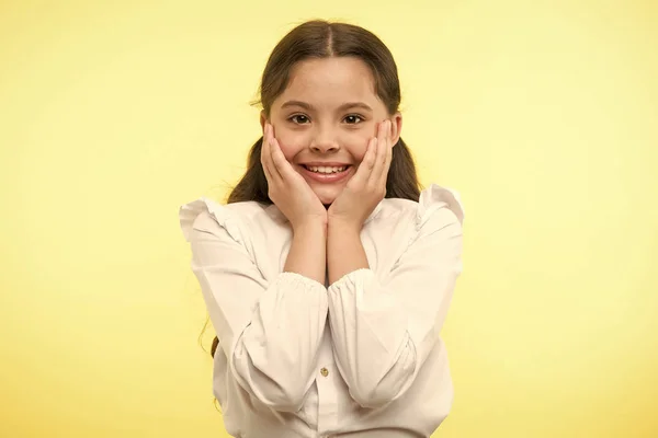 Lleno de emoción. Chica feliz cara sonriente toca sus mejillas de fondo amarillo. La colegiala no puede esperar a volver a la escuela. Esperando septiembre. Alumno emocionado por volver a la escuela —  Fotos de Stock