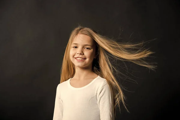 Liten flicka leende med långa blonda hår på svart bakgrund. Glada barn med mode frisyr. Skönhet kid leende med bedårande utseende. Skönhetssalong. I denna salong älskar vi hår — Stockfoto