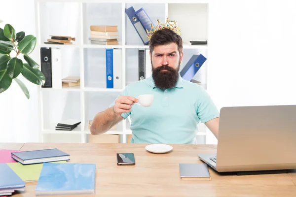 King of office. Head of department. Head office concept. Man bearded manager businessman entrepreneur wear golden crown on head. Relaxed top manager drinking coffee. Confident boss enjoying his glory