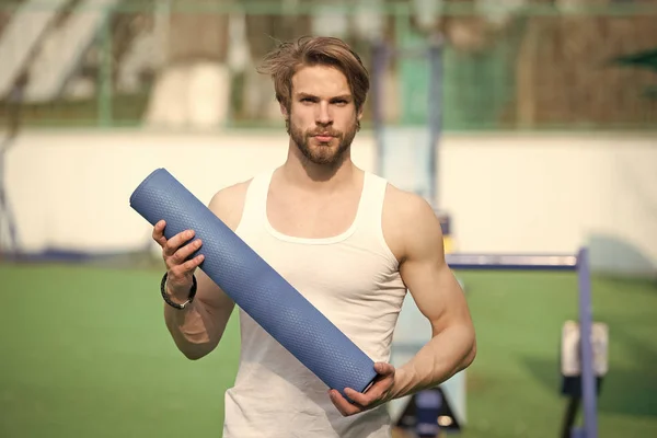 Practicing yoga. Sportsman carries yoga mat for outdoor practicing. Outdoor yoga concept. Man athlete confident face carries mat, going to stretching. Athlete always stretching after workout