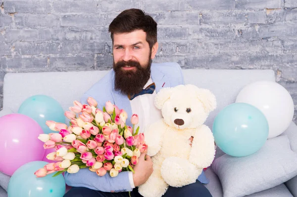 Macho ready romantic date. Man wear blue tuxedo bow tie hold flowers bouquet. Romantic man with flowers and teddy bear sit on couch waiting girlfriend. How successfully ask her dating. Romantic gift — Stock Photo, Image