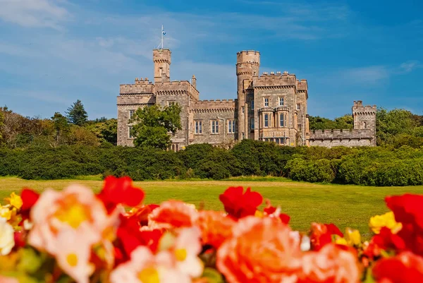 Lews Castle em Stornoway, Reino Unido, com rosas borradas em primeiro plano. Castelo com terreno verde no céu azul. Arquitetura histórica e design. Marco e atração. Férias de verão na ilha — Fotografia de Stock