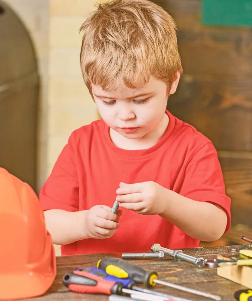 Closeup kid playing with metal bolts. Little laborer in workshop. Cute boy in red T-shirt behind the table — Stock Photo, Image