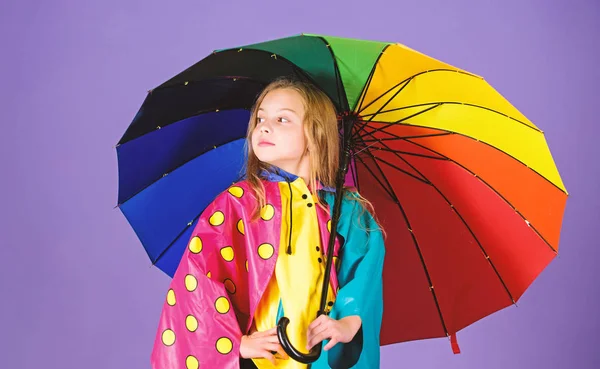 Mädchen glücklich halten bunten Regenschirm tragen wasserdichten Mantel. wasserfestes Zubehör für Kinder. Regenwetter mit passender Kleidung genießen. wasserdichtes Zubehör macht Regentag fröhlich und angenehm — Stockfoto