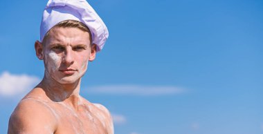 Şef katı yüz, gökyüzü arka plan üzerinde beyaz şapkalı. Kas gövde un ile kaplı olan adam çekici görünüyor. Seksi Şef kavramı. Adam çekici görünümü ile inşaat aşçı veya baker, kopya alanı