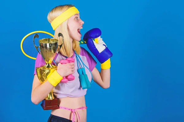 Sport equipment store. Sport for every day. Sport shop assortment. Girl successful modern woman hold golden goblet of sport champion and equipment blue background. How to find time for everything
