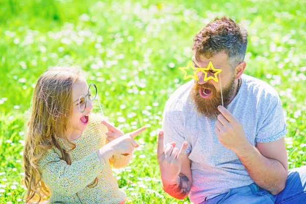 Tata i córka siedzi na trawie o trawnik, zielone tło. Dziecko i ojca pozowanie z eyeglases photo booth atrybut podczas mówienia. Pojęcie negocjacji. Rodzina spędzić aktywny wypoczynek na świeżym powietrzu — Zdjęcie stockowe