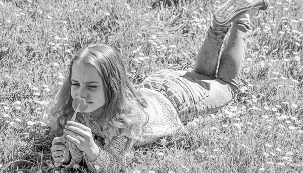 L'enfant profite du parfum de la tulipe tout en étant couché au pré. Concept d'allergie. Fille aux cheveux longs couché sur la prairie, fond d'herbe. Fille sur le visage souriant tient la fleur de tulipe rouge sur le jour ensoleillé du printemps — Photo