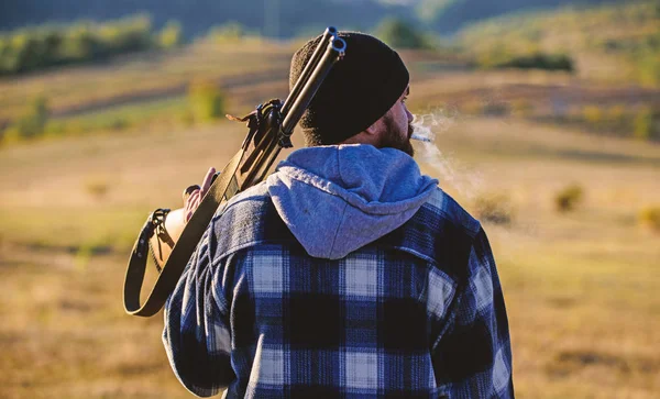 Hunter carry rifle gun on shoulder rear view. Guy hunter spend leisure hunting. Hunting masculine hobby leisure concept. Man brutal guy gamekeeper in hat nature background. Brutality and masculinity
