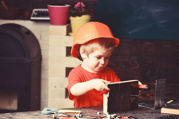 オレンジ色のハード帽子やヘルメット、研究室のバック グラウンドで少年を子供します。建築や建物内の将来のキャリアについて夢を見ている子。小児のコンセプト。少年は、ビルダーまたは修理としてプレイするツール — ストック写真