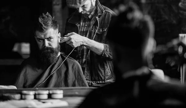 Hipster client getting haircut. Barber with clipper trimming hair on nape of client. Hipster hairstyle concept. Barber with hair clipper works on haircut of bearded guy barbershop background