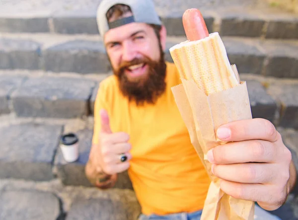 Homem barbudo desfrutar rua comida escadas fundo. Hipster come cachorro-quente e bebe café. Conceito da hora do almoço. Hipster desfrutar de cachorro-quente e beber bebida copo de papel. Fast food para almoço ideia comum — Fotografia de Stock