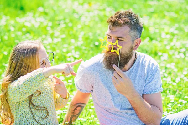 İletişim kavramı. Baba ve kızı, grassplot, arka planı yeşil çimenlerin üzerinde oturur. Aile açık havada eğlence harcamak. Çocuk ve babası eyeglases photo booth özniteliği ile konuşurken poz