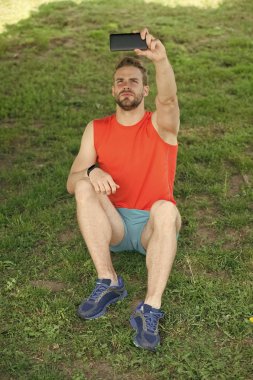 Yeni teknoloji ve modern yaşam. Maço sit smartphone ile yeşil çimenlerin üzerinde. Yaz etkinliği ve spor. Adam olun selfie cep telefonu ile temiz hava. Sporcu eğitim sonra sakin ol. Spor ve fitness