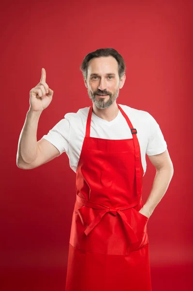 Kulinariska magi. Laga mat med skägg och mustasch iklädd förkläde röd bakgrund. Man mogen koka poserar matlagning förkläde. Chief cook och professional kulinariska. Laga mat hemma. Fina recept. Idéer och tips — Stockfoto