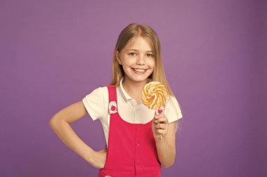 Parlak lolipop gülümseyen hamile. Pembe kıyafeti üzerinde mor arka plan izole uzun sarı saçlı kız. Tatlıya mutlu yüz büyük holding ile yuvarlak şeker, tatlı zaman kavramı