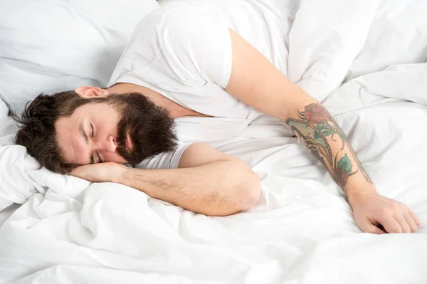 Lusta délelőtt. Az ember szakállas csípő álmos az ágyban. Kora reggeli órákban. Álmatlanság és problémák. Pihenni és aludni koncepció. Az ember szakállas fickó alvás, fehér lapokon. Egészséges alvás és a jólét — Stock Fotó