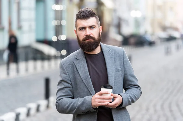 Homme barbu hipster boire tasse de papier café. Homme d'affaires bien entretenu profiter d'une pause café en plein air fond urbain. Pensée mais détendue. Marchez et dégustez du café chaud frais. Impliqué dans la relaxation — Photo