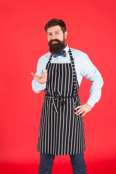 Profissional na cozinha. Homem com avental de hipster de barba. Hipster chef cozinhar fundo vermelho. Homem barbudo cozinheiro chef. Hipster cozinhar casa ou restaurante. Conceito moderno de café. Cozinhar refeições modernas — Fotografia de Stock