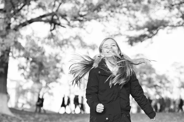 Speelse jongen vrije tijd. Kind blonde lange haren lopen in warme jas buiten. Meisje in de rode jas gelukkig genieten van Val natuurpark. Kind draag modieuze jas met capuchon. Vallen van kleren en mode concept — Stockfoto
