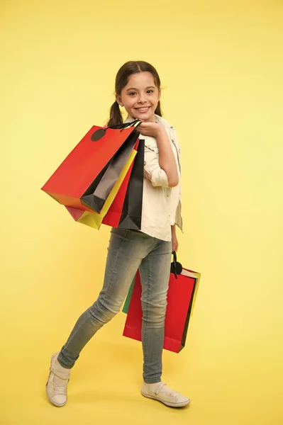 Változtatni az én stílusom. Gyermek aranyos fashionista bevásárló. A gyerek boldog shopping mall. Gyerek lány boldog mosolygó arc hordozza csomó csomagok sárga háttéren. Shopaholic lány szeret bevásárló vásárlás ruházat — Stock Fotó