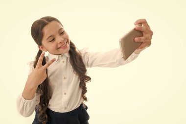 Genç vlogger akışı çevrimiçi. Çocuk okulu üniforması zeki çocuk gülen surat. Şirin, uzun kıvırcık saçlı bir kız akıllı telefon tutuyor ve selfie beyaz arka plan çekiyor. Çocuk okulu üniformaları akıllı telefon bulundurur.