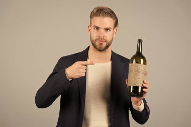 Bunu denemelisin. Adam şişe alkol içki tutar. Sosyal ve kültürel açıdan içme. İşadamı resmi takım elbise güvenle gri arka plan ağırlamaktadır. Adam misafirperver sunan şişe alkol