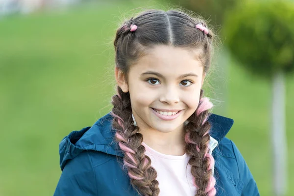 Cute smile. Fashionable hairstyle for kids. Girl small kid with fashionable braids hairstyle. Fashion trend. Salon and hair care. Girl cute smile face outdoors. Pleasant walk in park. Smile and joy