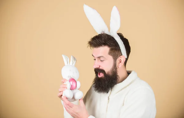 Birth and renewal. Easter bunny delivering colored eggs. Hipster with long rabbit ears holding egg laying hare. Bearded man with bunny toy and Easter egg. Celebration of spring time holiday