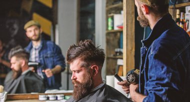 Hipster yaşam tarzı kavramı. Kuaför Saç kurutma makinesi ile saç modeli sakallı adam berber arka plan için çalışır. Hippi saç modeli almak istemci sakallı. İstemci saç kurutma saç kurutma makinesi ile berber