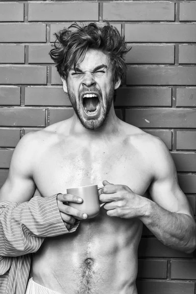 Hombre con barba beber café ladrillo fondo de la pared. El tipo tiene té o taza de café. Atleta cara somnolienta pelo acariciado desgaste albornoz mantenga taza. Macho sexy torso disfrutar del café. Concepto de café mañana — Foto de Stock