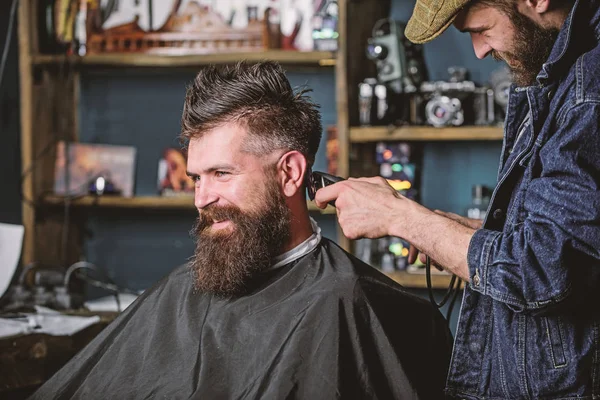 Barber with clipper trimming hair on nape of client. Barber with hair clipper works on haircut of bearded guy barbershop background. Hipster client getting haircut. Hipster hairstyle concept