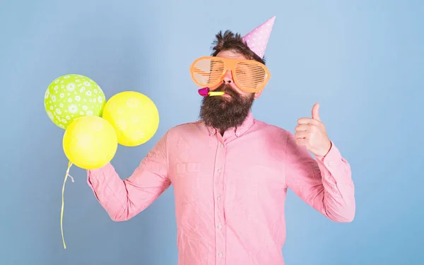 Artysta rozrywki kids party, obchody dnia międzynarodowych dzieci. Brodaty mężczyzna z ogromnymi okularami, wistle i balony, fajna koncepcja. Hipster z modnych brodą w różowej koszuli na niebieskim tle — Zdjęcie stockowe