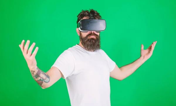 Koncepcja wyższości. Hipster na poważnej twarzy podnosi ręce, ciesząc się wyższością w wirtualnej rzeczywistości. Facet z wyświetlaczem montowanym na głowie wchodzi w interakcję w VR. Mężczyzna z brodą w okularach VR, zielone tło — Zdjęcie stockowe