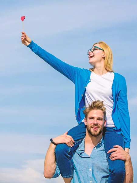 Man bedriver flickvän axlar, himmel bakgrund. Par lyckliga datum att ha roligt tillsammans. Kvinna håller hjärta på pinne symbol för kärlek. Par i kärlek promenader utomhus solig dag. Romantisk datum koncept — Stockfoto