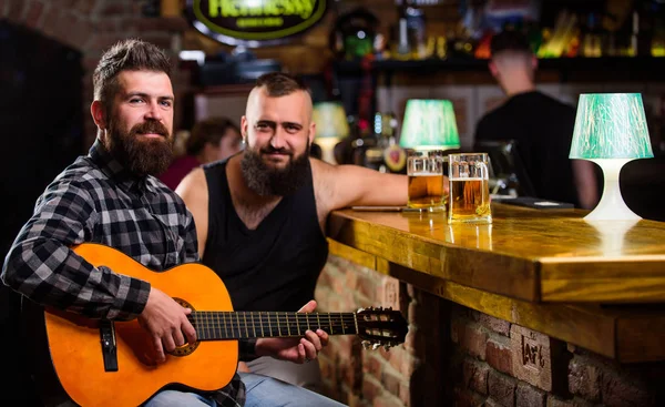 Real men leisure. Man play guitar in bar. Cheerful friends relax with guitar music. Friday relaxation in bar. Friends relaxing in bar or pub. Hipster brutal bearded spend leisure with friend in bar