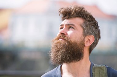 Hipster sakal ve bıyık sıkı yüzündeki defocused gökyüzüne, kentsel arka plan, görünüyor. Sakallı adam güneşli hava keyfini çıkarın. Sakallı adam gökyüzü güneşli günde görünüyor. Hava tahmini kavramı