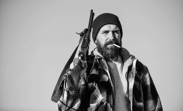 Hunter with rifle gun close up. Guy bearded hunter spend leisure hunting and smoking. Brutality and masculinity. Hunting masculine hobby concept. Man brutal bearded guy gamekeeper blue sky background