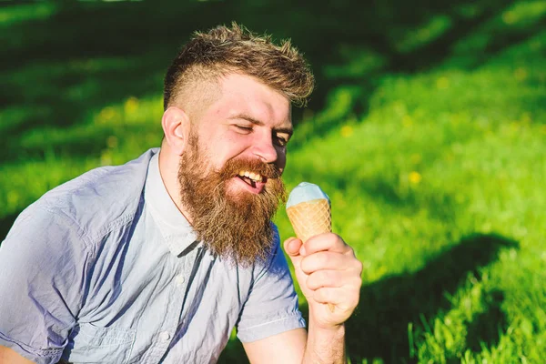 Homem com barba e bigode no rosto feliz come sorvete, grama no fundo, desfocado. Homem com barba longa desfrutar de sorvete, enquanto se senta na grama. Conceito de delicadeza. Homem barbudo com cone de sorvete — Fotografia de Stock